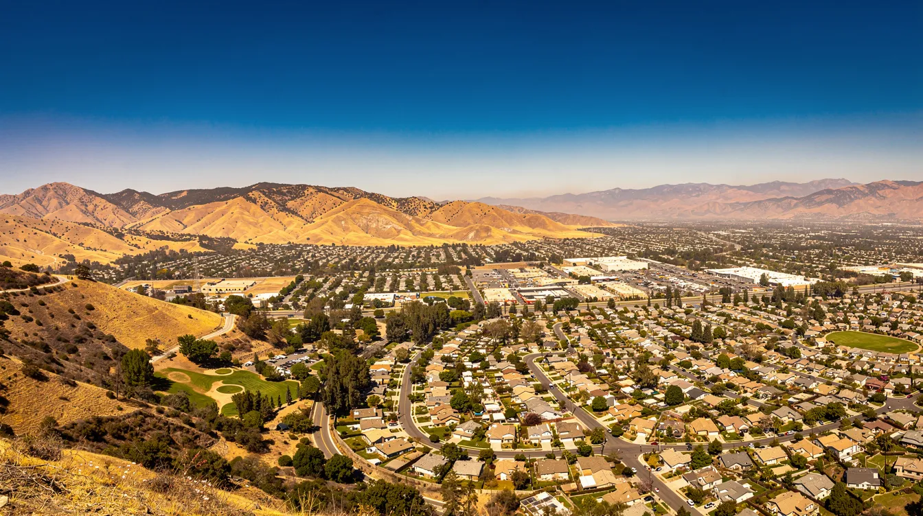 A panoramic view showcases a wide suburban valley, surrounded by dry, golden-brown mountains under a clear blue sky, highlighting the natural beauty of Simi Valley and its location within Southern California. This serene landscape reflects the community pride of Simi Valley residents and the area's Mediterranean climate.